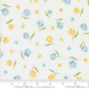 May include: White fabric with a repeating pattern of blue and yellow daisies and small floral accents. The flowers have green stems and leaves. The fabric has a ruler along the bottom edge.