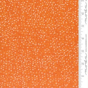 May include: A vibrant orange fabric featuring a dense pattern of small, light-colored dots scattered across a background of thin, intersecting dark orange lines. A white ruler is visible on the right edge, showing measurements in inches.
