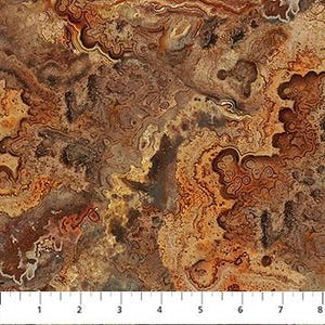 May include: Close-up of a fabric with a marbled pattern in shades of brown, tan, and gold. The design features swirling lines and organic shapes, resembling a cross-section of a stone. A ruler is at the bottom, with markings in inches.