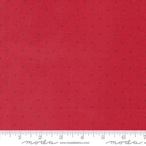 May include: Red fabric with small, evenly spaced brown dots. The fabric has a textured appearance and a ruler is visible along the bottom edge, marked with inches. The fabric is suitable for quilting and other craft projects.