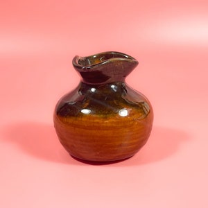 May include: A brown and black ceramic vase with a rounded body and a wide, slightly flared opening.