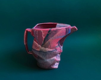 May include: A pink and blue ceramic pitcher with a unique, abstract design. The pitcher has a handle and a spout.