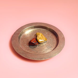 May include: Three heart-shaped stones, one red, one yellow, and one brown, are arranged on a silver tray with an ornate design.