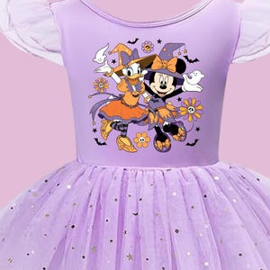 May include: A light purple dress with ruffled tulle sleeves and a layered tulle skirt featuring gold star accents. The bodice displays a graphic print of Daisy Duck and Minnie Mouse in orange and purple witch costumes surrounded by ghosts and bats.