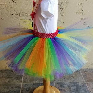 Puede incluir: Falda de tut&uacute; de tul arco&iacute;ris con una cintura de crochet roja. La falda est&aacute; hecha de varias capas de tul en tonos de morado, azul, verde, amarillo, naranja y rojo.