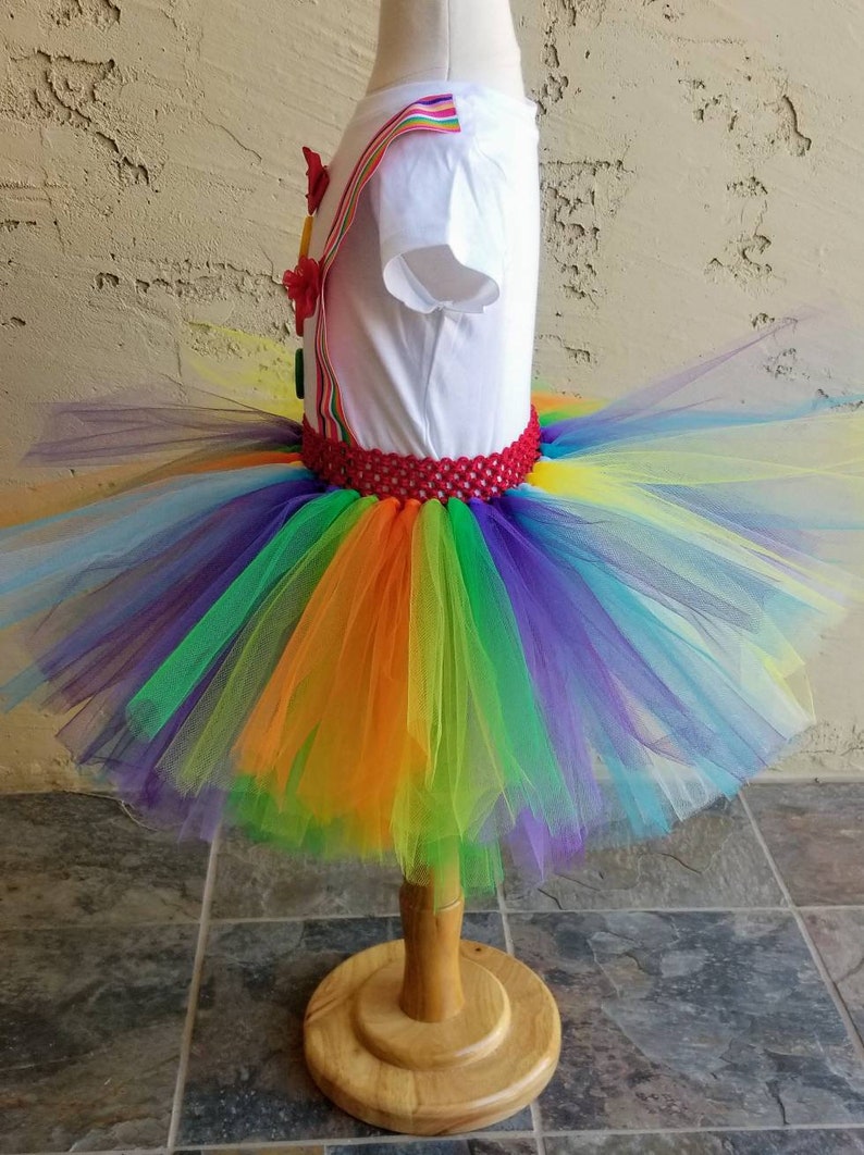 Puede incluir: Falda de tut&uacute; de tul arco&iacute;ris con una cintura de crochet roja. La falda est&aacute; hecha de varias capas de tul en tonos de morado, azul, verde, amarillo, naranja y rojo.