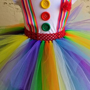 Puede incluir: Un tut&uacute; arco&iacute;ris con una camisa blanca con una pajarita roja y botones de colores. La camisa tiene tirantes arco&iacute;ris.