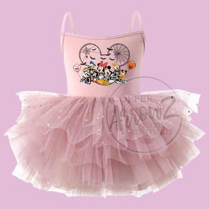May include: A light pink tutu dress with spaghetti straps. The bodice features a Halloween-themed graphic of Disney characters. The layered tulle skirt is adorned with gold star-shaped glitter, creating a whimsical effect. The dress is designed for children.
