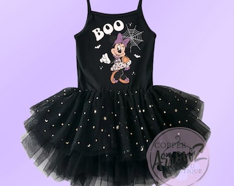 May include: Black tulle tutu dress with a black sleeveless top featuring a white "BOO" graphic and a cartoon image of Minnie Mouse dressed as a witch. The dress is decorated with gold glitter stars.