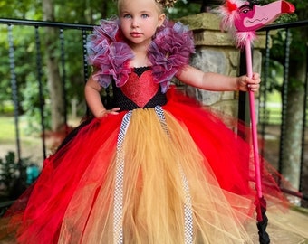 May include: A young girl dressed as the Queen of Hearts from Alice in Wonderland. She is wearing a red and gold tulle tutu, a black and red bodice with a large red heart, and a purple and blue ruffled collar. She is holding a pink flamingo croquet mallet.