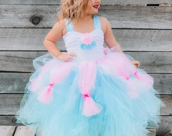Puede incluir: Una niña pequeña con un vestido de tul de color azul claro y rosa con un corpiño blanco y lazos rosas. Lleva una diadema con un lazo azul claro y tiene el pelo rubio rizado.