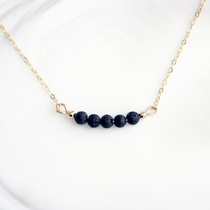 May include: A gold chain necklace with five black lava rock beads.