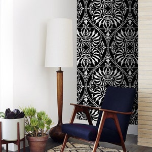 May include: A black and white patterned wallpaper with a white armchair in front of it. The armchair has a dark blue fabric seat and wooden legs.