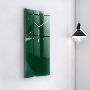 Puede incluir: Un reloj de pared rectangular con una superficie de cristal de color verde intenso. El reloj presenta finas marcas horarias blancas y manecillas blancas delgadas para las horas y los minutos. El diseño es plano y vertical.
