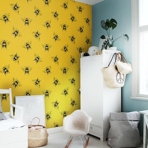 May include: A white rocking chair sits in a room with a yellow wall covered in a black bee pattern. A white dresser with a wicker basket hanging on the side is in the corner of the room.