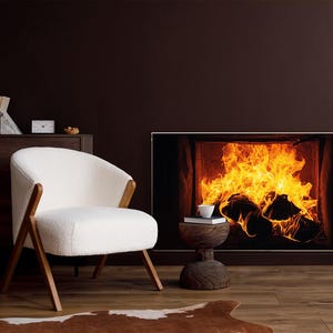 Op de afbeelding: Een gezellige interieurscène met een witte fauteuil, houten accenten en een decoratieve open haard met een vuurafbeelding. Een kleine bijzettafel met een kopje en boeken. De kamer heeft een warme, uitnodigende sfeer.
