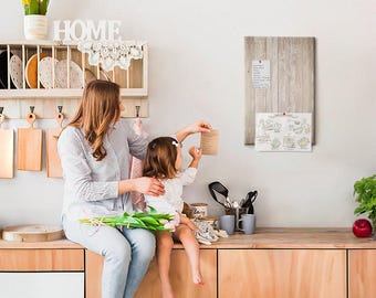 May include: A light-colored wooden wall-mounted plate rack with hooks holding three wooden cutting boards, a white HOME sign, and a gray wooden memo board with a pinned paper list and a printed illustration of kitchen items on a wall.
