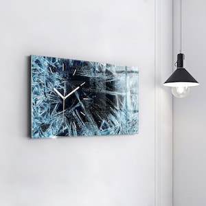 May include: A blue and black clock with a white face and hands, featuring a cracked ice design. The clock is mounted on a white wall.