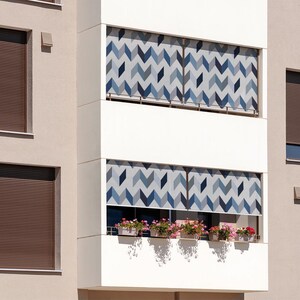 May include: A modern apartment building with brown window blinds and patterned balcony shades. The balcony has potted plants with flowers.