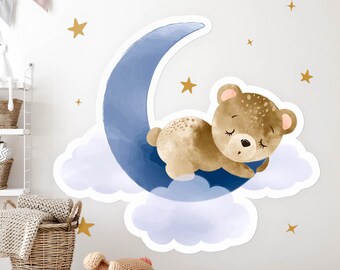 May include: A wall decal featuring a sleeping brown bear on a blue crescent moon, resting on a cloud. Gold stars are scattered around the bear and moon. The design is suitable for a nursery or children's room.