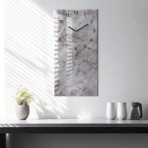 May include: A gray and white marble clock with black hands and black numbers. The clock is hanging on a white wall.