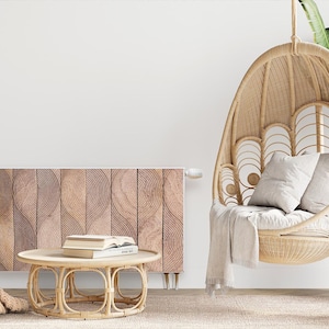 Könnte beinhalten: Ein weißer, runder, wandmontierter Thermostat mit einem Holzpaneel-Heizkörper dahinter. Im Vordergrund steht ein hängender Korbstuhl mit einer weißen Wolldecke und Kissen. Ein kleiner Korbtisch mit Büchern darauf steht vor dem Heizkörper.
