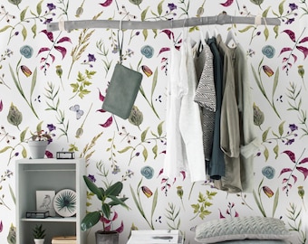 Op de afbeelding: Een witte muur met een bloemenbehang met een herhalend patroon van groene bladeren, paarse bloemen en rode stengels. Een houten plank met een kleine potplant, boeken en een decoratief bord bevindt zich aan de linkerkant van de afbeelding. Een kledingrek met verschillende kledingstukken die eraan hangen bevindt zich aan de rechterkant van de afbeelding. De muur is versierd met een bloemenbehang.