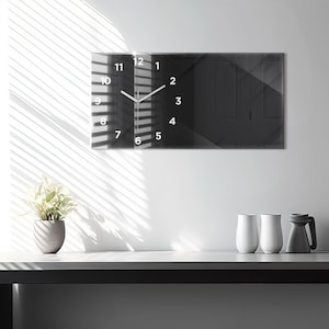 May include: A black and white clock with a mirrored face and white numbers. The clock is hanging on a white wall with a window behind it. The clock is in a modern style.