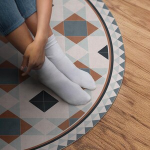 May include: A round rug with a geometric pattern in shades of blue, brown, and white. The rug has a white background with a repeating pattern of triangles and squares.