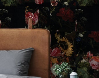 May include: A brown leather headboard with a gray duvet cover and a bedside table with a green plant and a decorative bottle. The wall behind the bed is covered in a floral wallpaper with a black background and colorful flowers.
