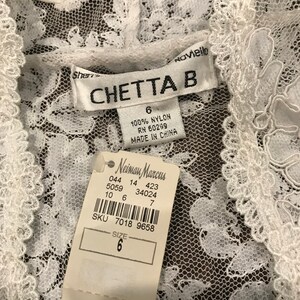 May include: A white lace garment with a tag from Neiman Marcus. The tag indicates the size is 6 and the garment is made of 100% nylon. The brand name "CHETTA B" is visible on a label.