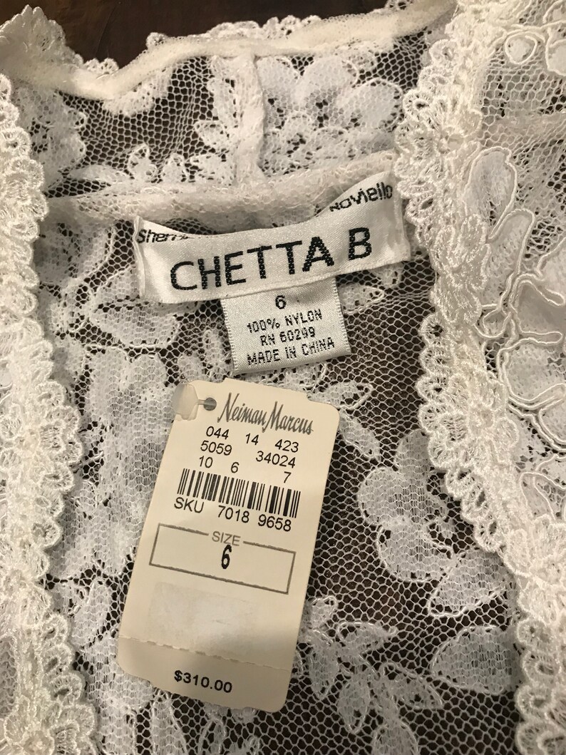 May include: A white lace garment with a tag from Neiman Marcus. The tag indicates the size is 6 and the garment is made of 100% nylon. The brand name "CHETTA B" is visible on a label.