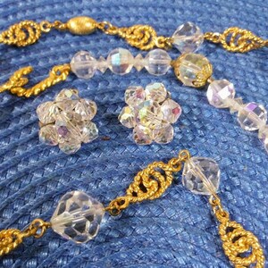 May include: A gold chain necklace with clear crystal beads and matching earrings. The necklace has a twisted gold chain design and the earrings are small and round.