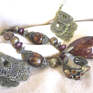 May include: A set of jewelry featuring a necklace with brown and gold beads, a ring with amber stones, and a pair of earrings with a filigree design.