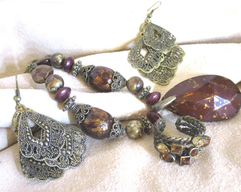 May include: A set of jewelry featuring a necklace with brown and gold beads, a ring with amber stones, and a pair of earrings with a filigree design.