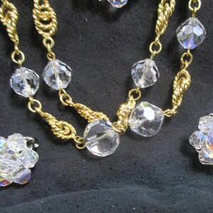 May include: A gold chain necklace with clear crystal beads and matching earrings. The necklace has a twisted chain design.