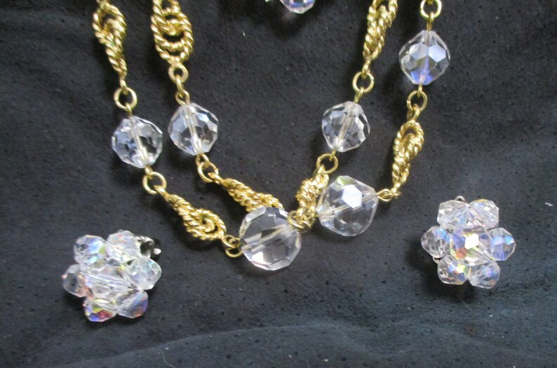 May include: A gold chain necklace with clear crystal beads and matching earrings. The necklace has a twisted chain design.