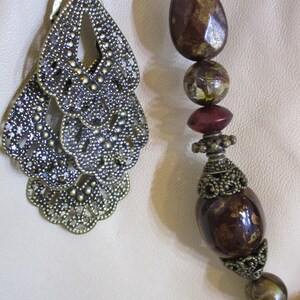 May include: A close-up of a necklace with a large, ornate, bronze pendant and brown, red, and gold beads.