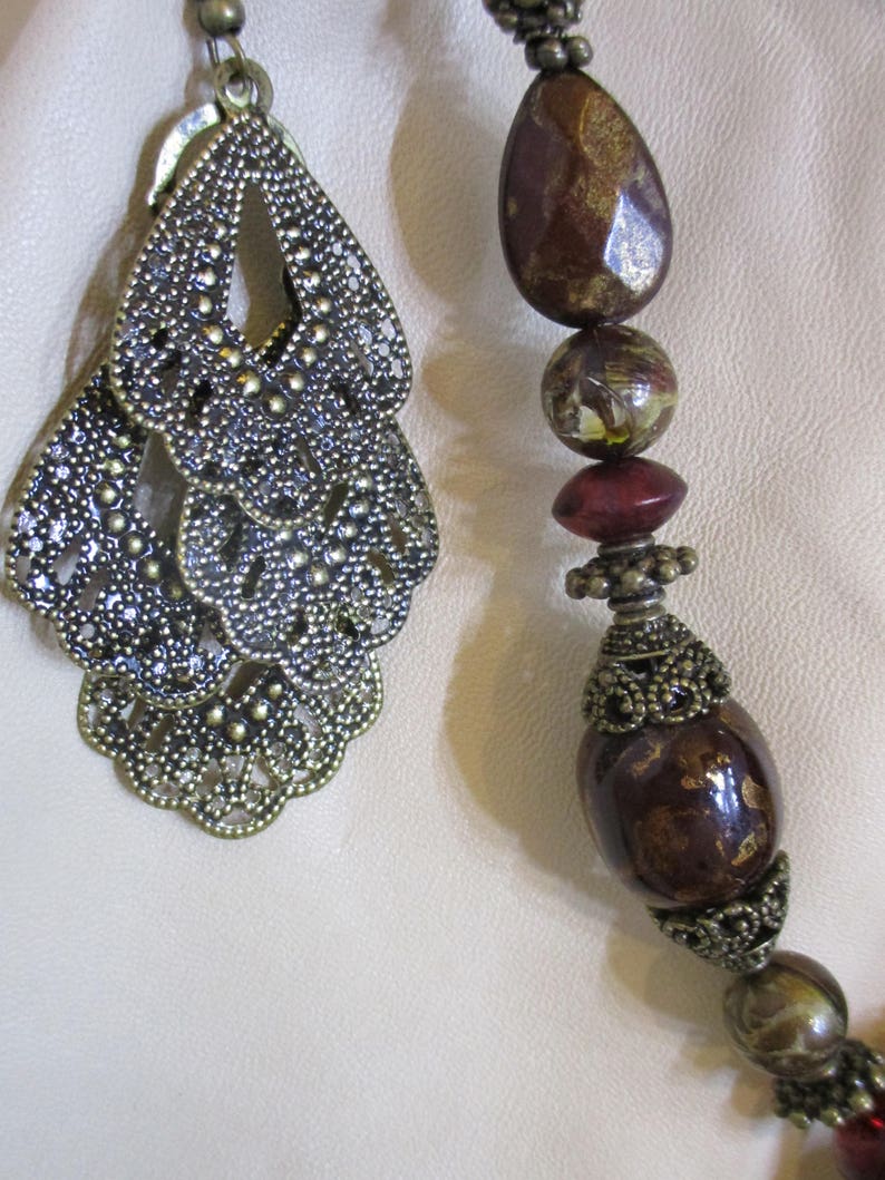 May include: A close-up of a necklace with a large, ornate, bronze pendant and brown, red, and gold beads.
