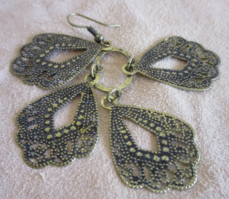 May include: A pair of gold-tone dangle earrings with a delicate, intricate design. The earrings feature multiple teardrop-shaped charms with a cutout pattern.