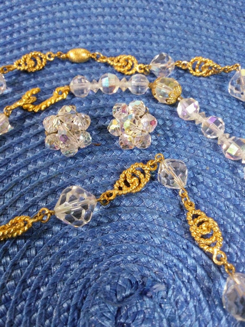 May include: A gold chain necklace with clear crystal beads and matching earrings. The necklace has a twisted gold chain design and the earrings are small and round.