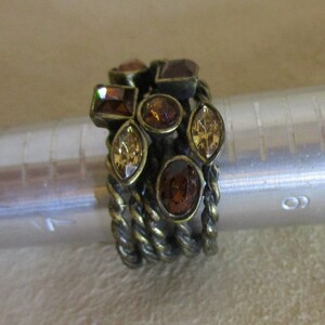 May include: A gold-toned ring with a twisted band and multiple brown and gold-colored rhinestones.