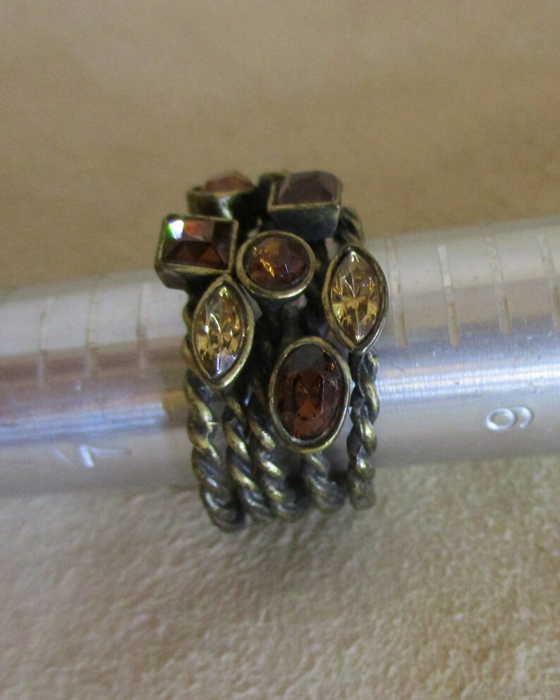 May include: A gold-toned ring with a twisted band and multiple brown and gold-colored rhinestones.