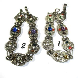 May include: Two silver bracelets with colorful enamel and rhinestone accents. The bracelets are labeled "1" and "2".