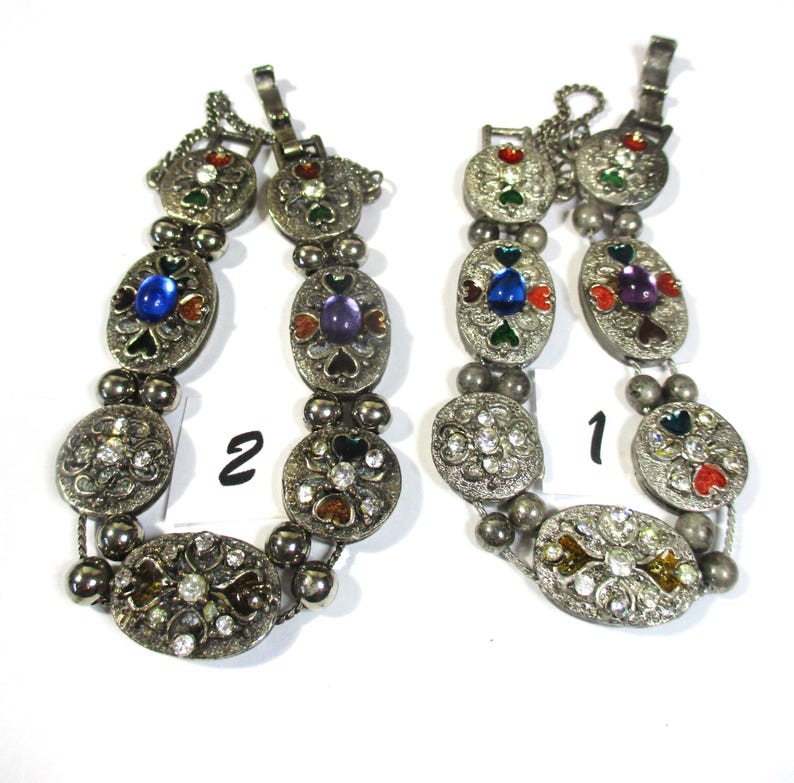 May include: Two silver bracelets with colorful enamel and rhinestone accents. The bracelets are labeled "1" and "2".