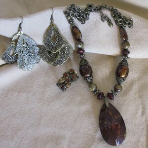 May include: A set of jewelry featuring a brown and gold necklace with a large teardrop pendant, a pair of dangle earrings with a filigree design, and a ring with a cluster of brown and gold stones.