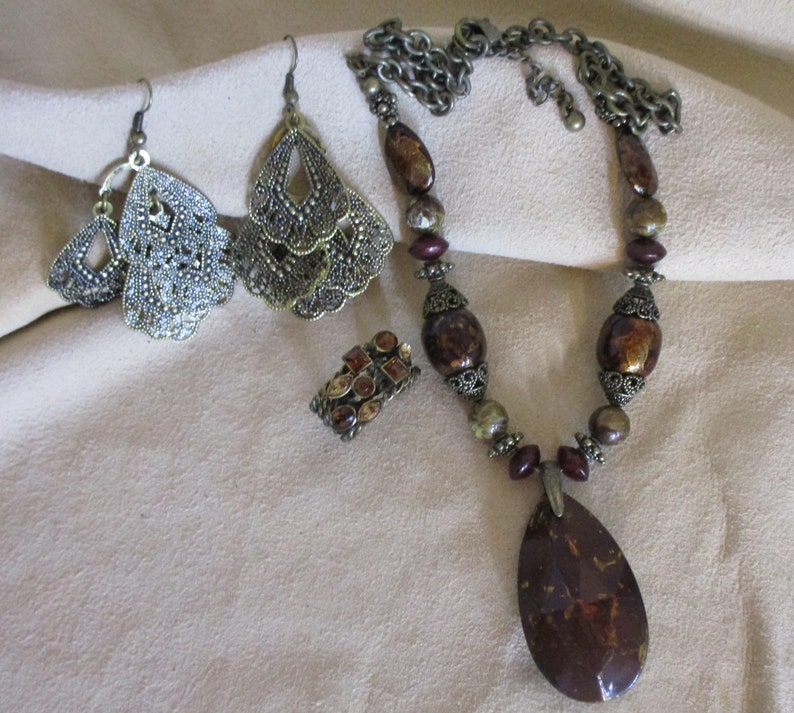 May include: A set of jewelry featuring a brown and gold necklace with a large teardrop pendant, a pair of dangle earrings with a filigree design, and a ring with a cluster of brown and gold stones.