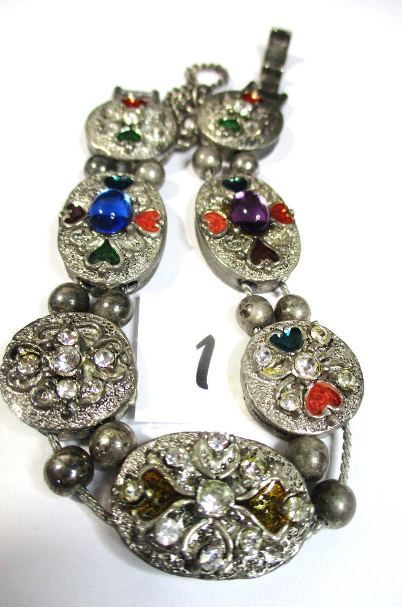 May include: A silver bracelet with multiple oval-shaped charms. Each charm is decorated with colorful enamel and rhinestones. The charms are connected by a silver chain and silver beads.