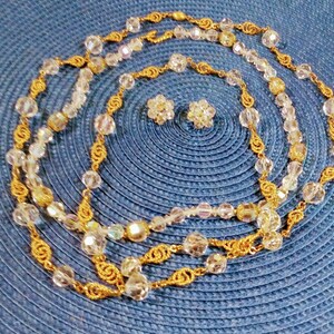 May include: A gold chain necklace with clear crystal beads and matching earrings. The necklace is layered and has a delicate design.
