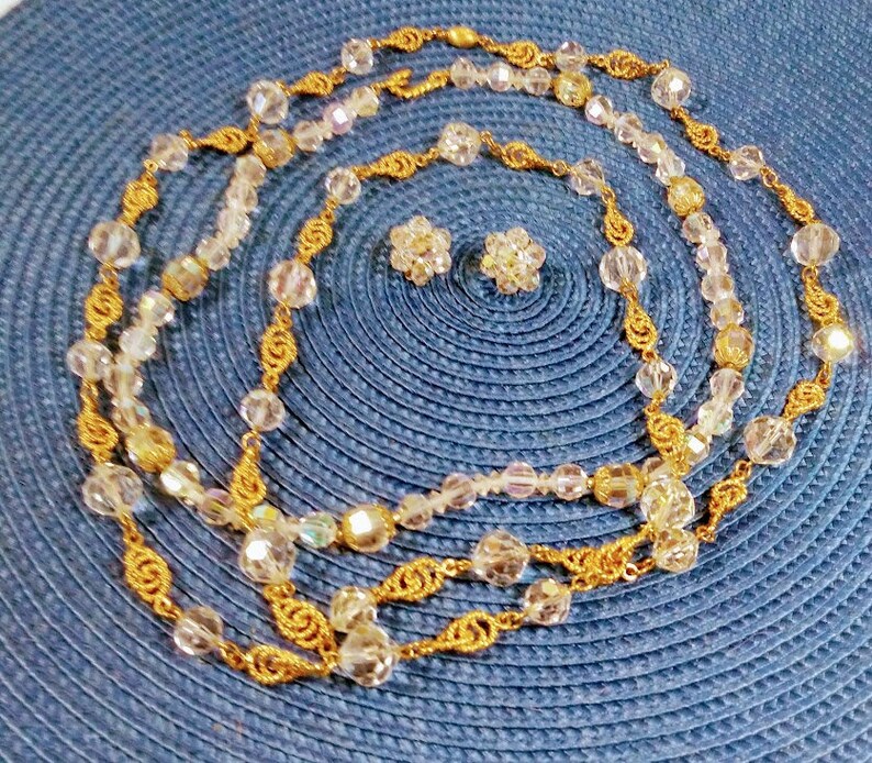May include: A gold chain necklace with clear crystal beads and matching earrings. The necklace is layered and has a delicate design.